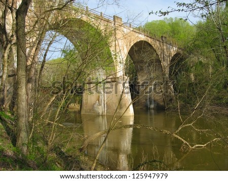 An old bridge across a stream in the springtime with trees just beginning to bloom.