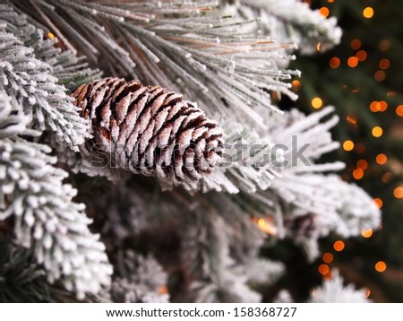 A snowy pinecone decorated Christmas tree, with bokeh lights in the background.