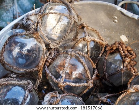 A large metal bucket filled with clear glass fishing floats all wrapped in rope netting.