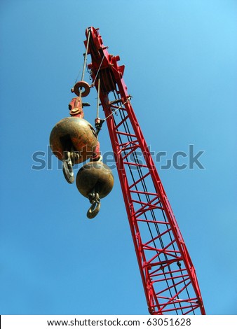 Two wrecking balls suspended from a red crane, high above the ground, against a blue sky background.