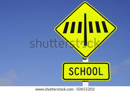 Zebra crossing sign with school set against blue sky
