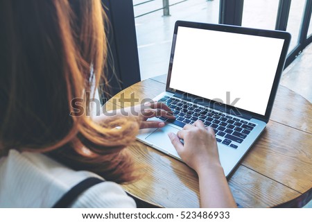 Mockup image of a woman using laptop with blank white screen on wooden table in modern cafe