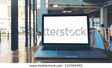 Laptop with blank white screen on wooden table in modern cafe