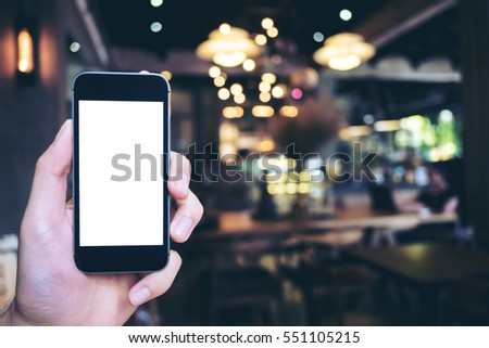 Mockup image of hand holding black mobile phone with blank white screen in cafe