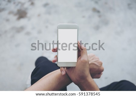 Mockup image of a man sitting on the street and holding white mobile phone with blank white screen
