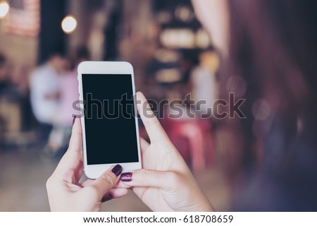 Mockup image of a woman holding mobile phone with blank black screen in modern loft cafe