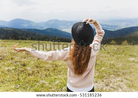 young girl looking into the distance, beautiful mountains in the background, thinking deeply, wearing pink jacket and hat, nature, traveling, brown long hair
