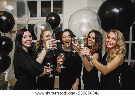 Cheers!Crazy party time of  beautiful stylish women in elegant casual black outfit celebrating new year, birthday,having fun,dancing,drinking alcohol cocktails. Black and gold Balloons on Background.