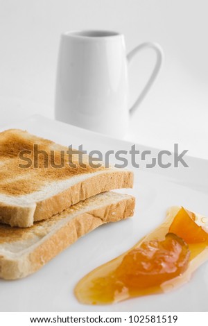 two of toast, peach jam on a white plate and a coffee  cup in the background