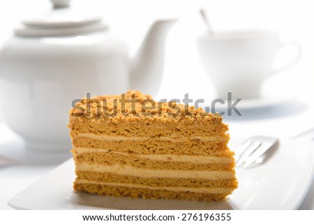 piece of honey cake on a white plate, teacup and teapot