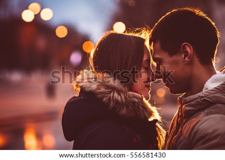 Portrait of young beautiful couple kissing in an autumn rainy day. Filtered with grain and light flashing
