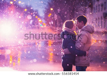 In love couple kissing in the snow at night city street. Filtered with grain and light flashing