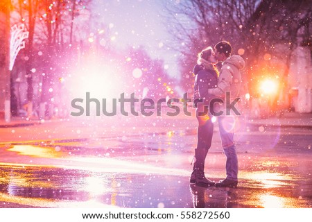 In love couple kissing in the snow at night city street. Filtered with grain and light flashing
