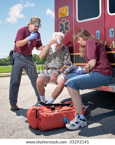 Two EMTs review a patients injuries while sitting on the back step of the ambulance