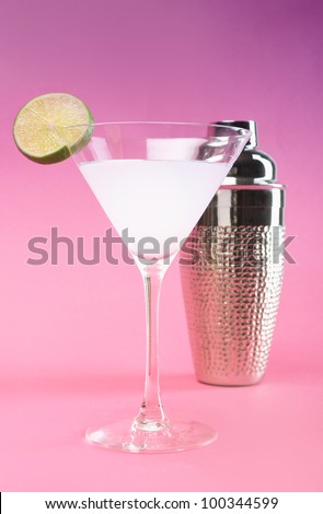 White cocktail with lime and shaker on pink background