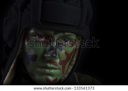 Female Soldier in a Tank Helmet With Face Camouflage Against Dark Background