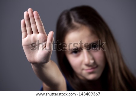A young girl putting up her hand, to say no, or stop, with a serious frowned expression.