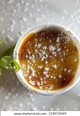 Creme brulee with mint on white plate, dusted with castor sugar.