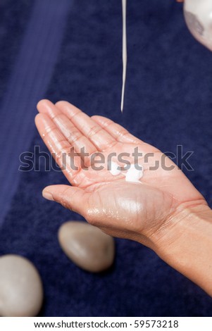 Massage oil and cream dripped into hand, with a blue towel background.