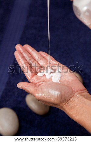 Massage oil and cream dripped into hand, with a blue towel background.