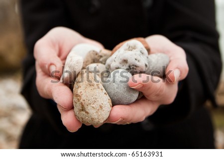 Caucasian hands holding pebbles found on the beach towards the camera.