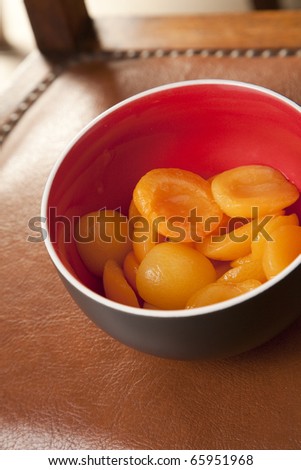 Bowl of peach halves in syrup on a leather chair seat.