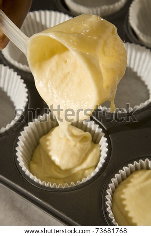 Vanilla cake-mix being poured into cupcake forms