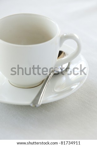A white cup and saucer, empty, on a white table cloth