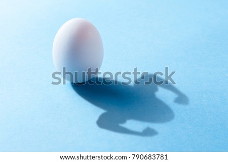 Chicken egg is rich in natural protein for muscle growth. The egg casts a shadow with the hands of the bodybuilder with the bicep. Blue background