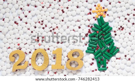 Happy New Year 2018 for medical and health concept. Christmas tree made form green medical capsule w/ gold wooden number 2018 text and decorative little stars on white pill background. Copy space.