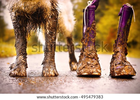 Muddy dog stands next to his owner with muddy boots