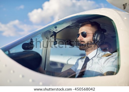 Portrait of cool young adult pilot sitting in private air plane ready to take off. Bright summer day, handsome male model