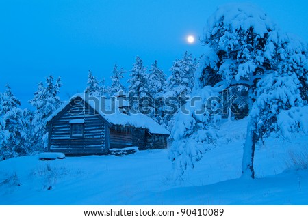 Cabin in the snow covered forest at night.