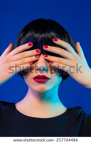 stylish brunette bob haircut closes her eyes with hands. red manicure. red lips