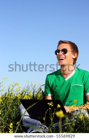 Laughing young man on a yellow field with a laptop