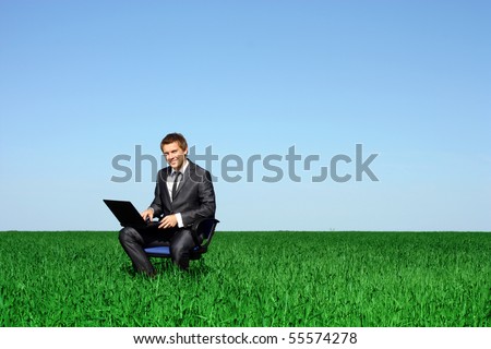 Happy man with laptop in the wheat field. Man sitting on the office chair