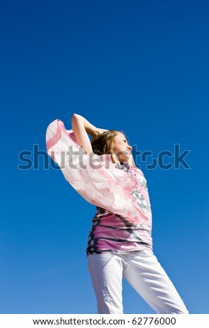 Happy young lady playing with her scarf near the sea, in the wind