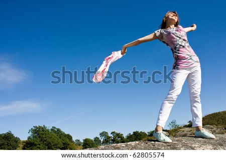 Happy young lady playing with her scarf near the sea, in the wind