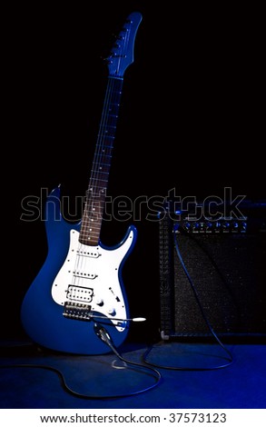 electric guitar and combo amplifier in rays of blue light on black background