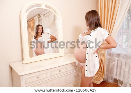 Young pregnant woman looks in a mirror and smiles