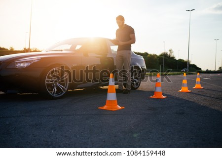 Driving school or test. Beautiful young woman with instructor learning how to drive and park car between cones.