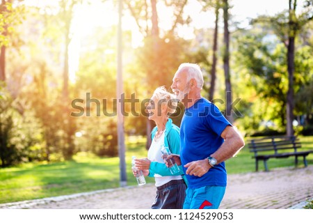 Happy senior couple jogging outdoors in park.