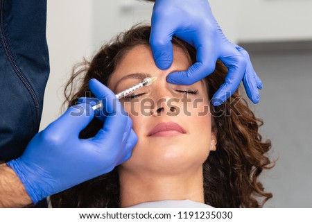 Close up of beautician expert\'s hands injecting botox in female forehead.