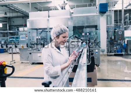Water factory - Water bottling line for processing and bottling pure mineral carbonated water into bottles. Female worker checking water bottles.