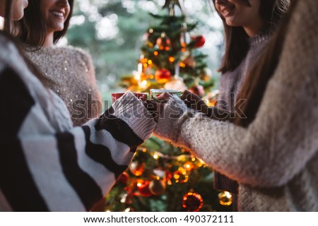 Friend celebrating together and holding cups of warm tea. Christmas tree in background. Selective focus.