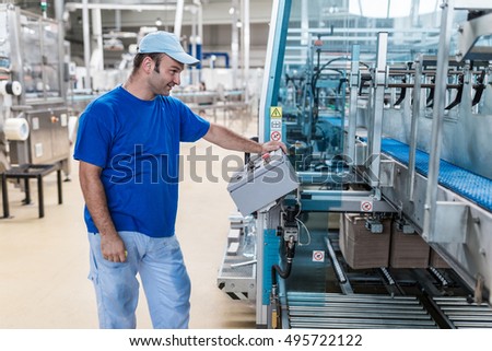 Happy smiled worker doing his job on Robotic factory line for processing and quality control in water factory.