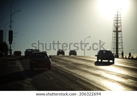 Backlit of a street with cars approaching the camera and a TV tower in the back