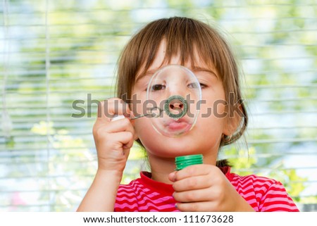 Beautiful little  girl blowing soap bubbles indoor