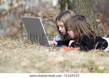 Two little girls playing on computer outside in autumn