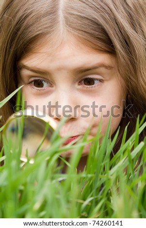 Cute little girl looking at grass through magnifying glass